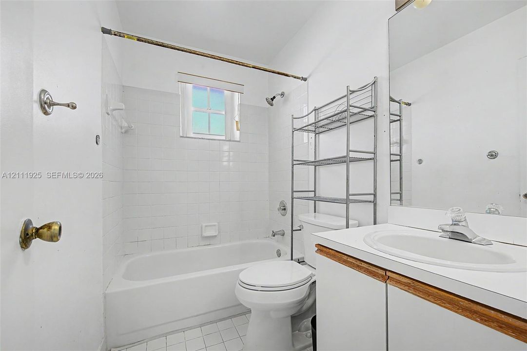 Bathroom featuring a white vanity with an integrated sink, large wall-mounted mirror, ceramic tile surround, and tub-shower combination