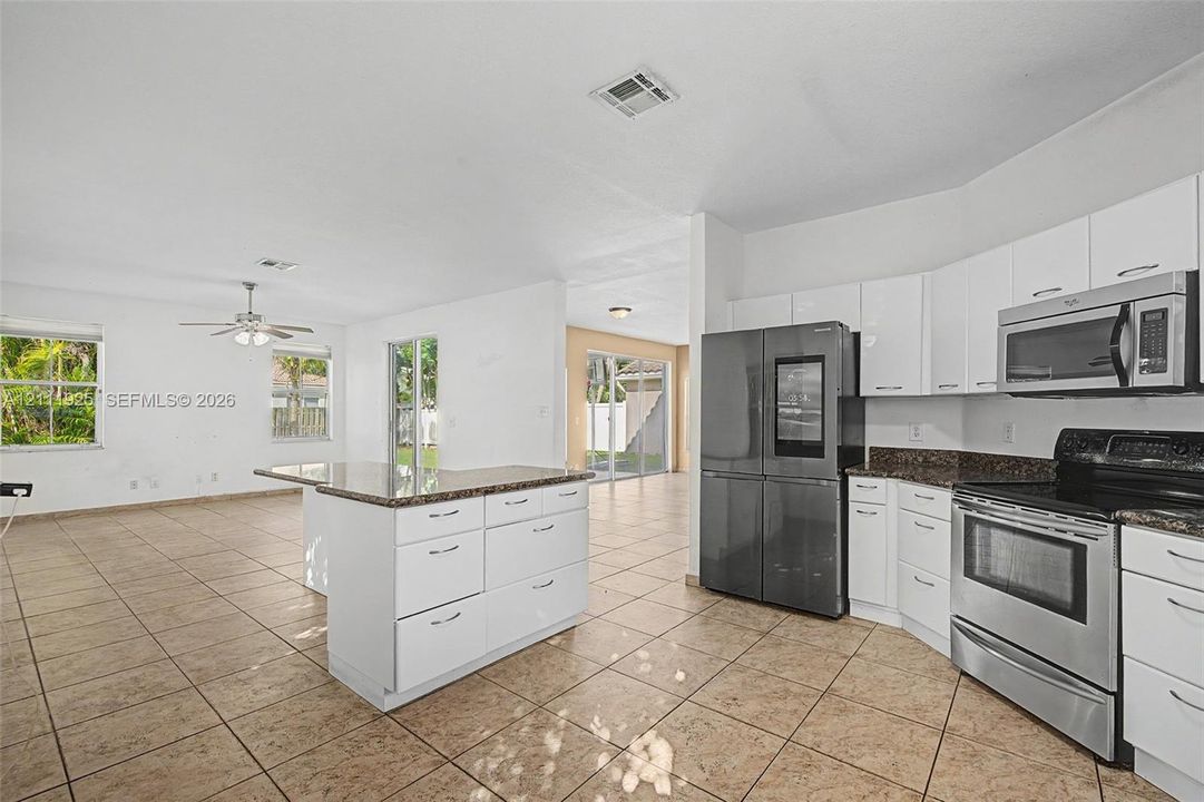 Kitchen featuring white shaker-style cabinetry, stone-finish countertops, stainless steel appliances, a center island, and ceramic tile flooring