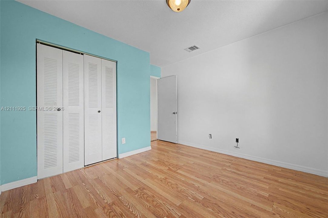 Room featuring wood-finish flooring, white walls, louvered bi-fold closet doors, and flush-mount ceiling lighting