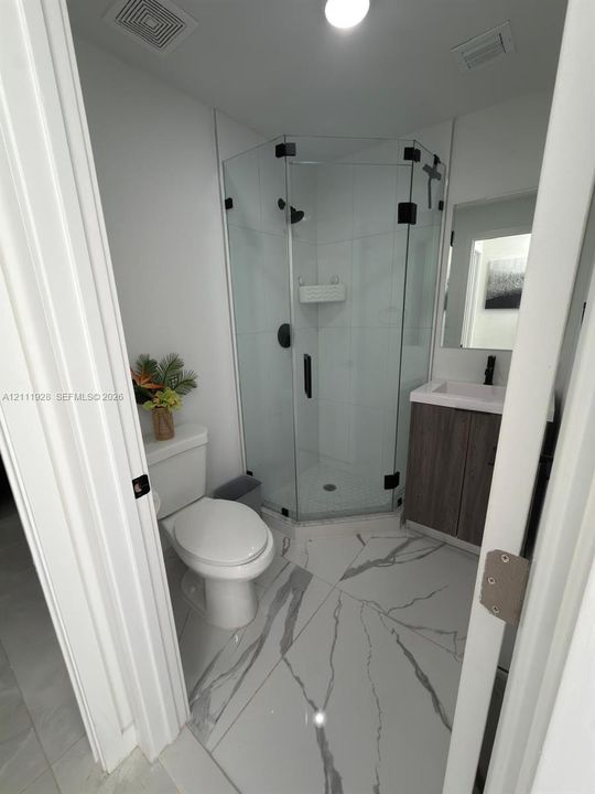 Corner shower stall with glass enclosure and matte black hardware, vanity with stone-pattern countertop, and large-format porcelain tile flooring