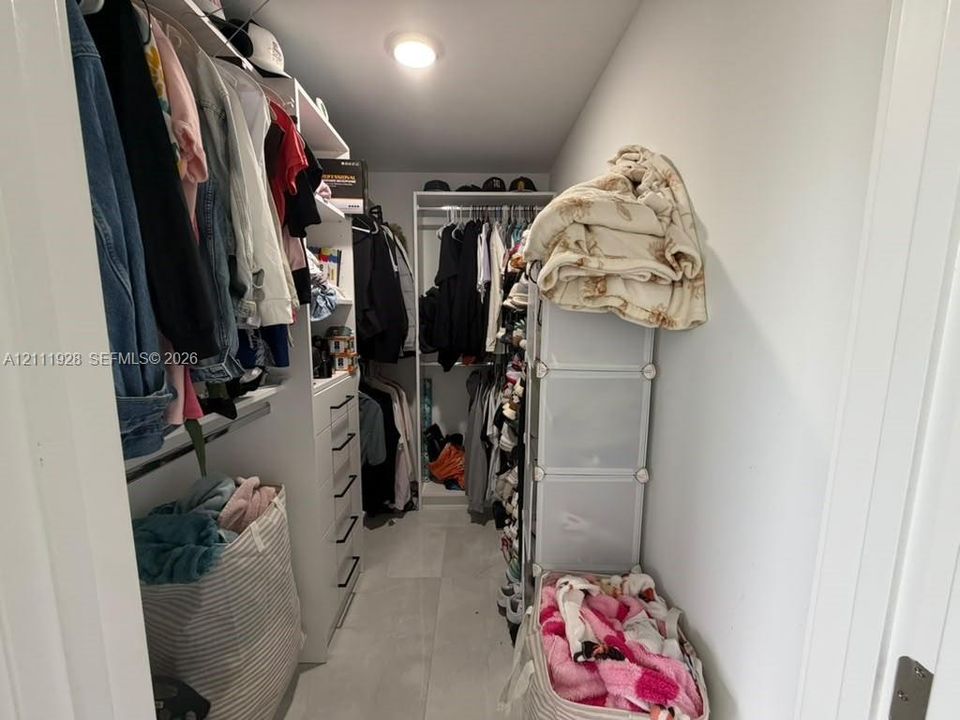 Walk-in closet featuring white built-in shelving, integrated dresser drawers with matte black hardware, and neutral-tone tile flooring