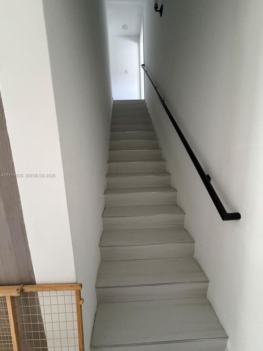 Staircase featuring wood-finish treads and a matte black wall-mounted handrail