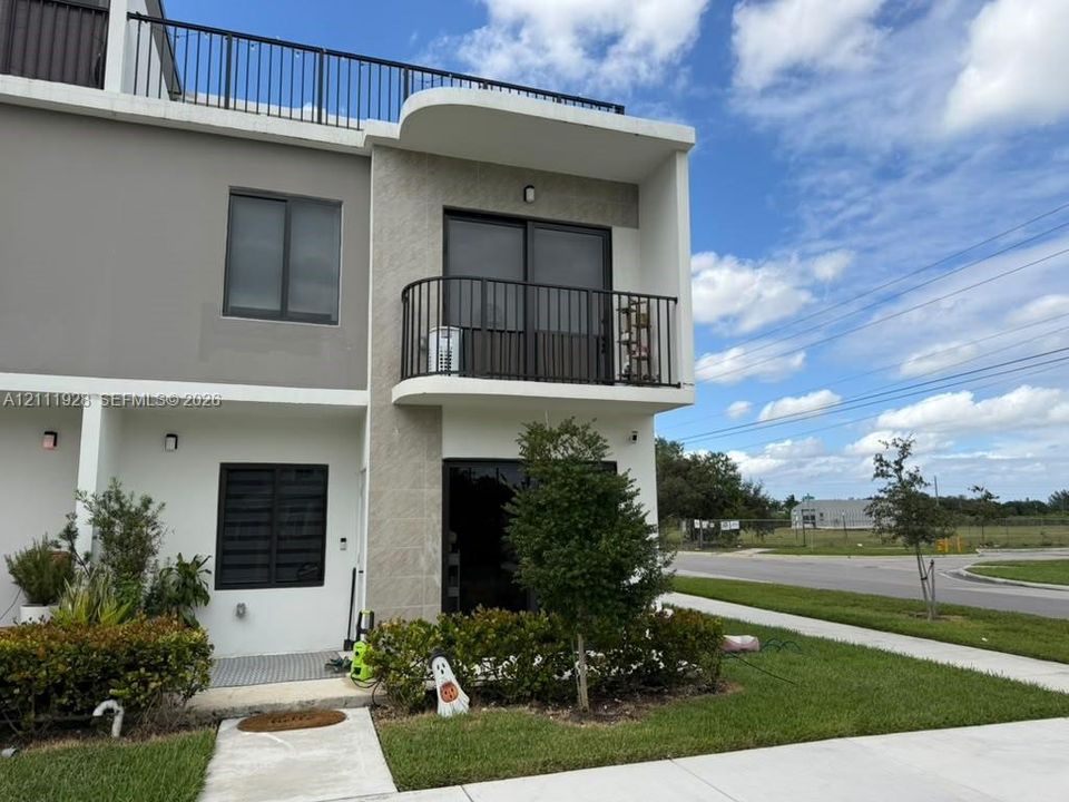 Contemporary townhome exterior featuring a second-level balcony, a rooftop terrace with metal railings, stucco facade, and stone-veneer accents