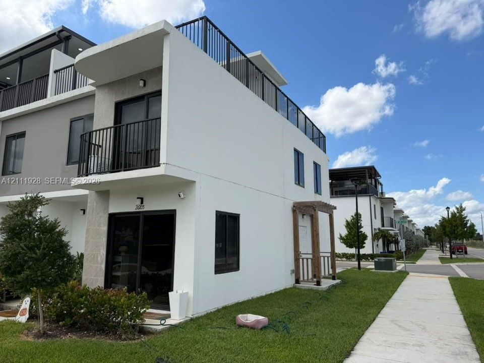 Modern townhome exterior featuring a rooftop deck with metal railings, a private second-story balcony, sliding glass doors, and a decorative wood-post entryway