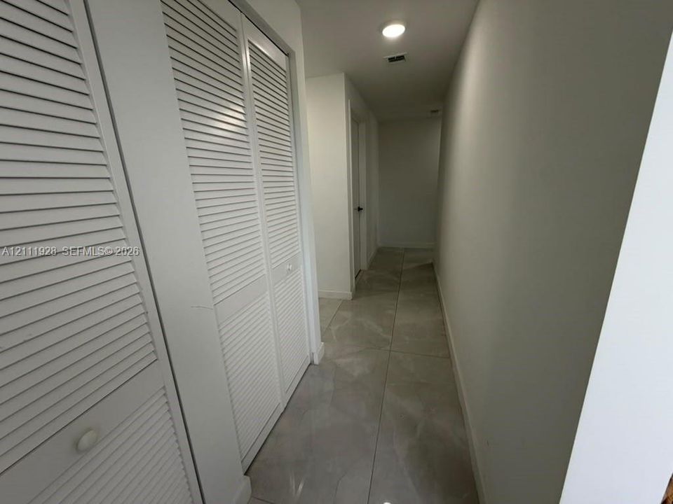 Hallway featuring large-format tile flooring and white louvered-door closet cabinetry
