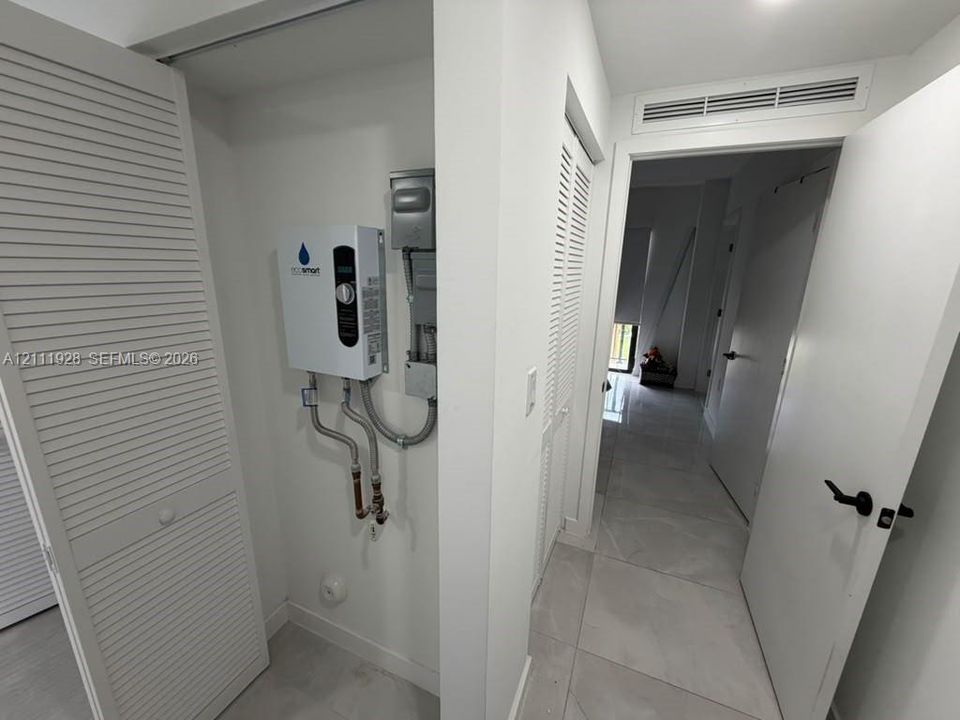 Utility alcove featuring a wall-mounted electric tankless water heater, white louvered closet doors, and large-format porcelain tile flooring