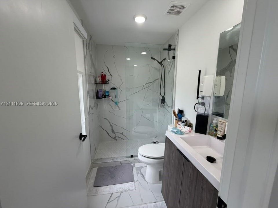 Walk-in shower with floor-to-ceiling stone-pattern tile, frameless glass enclosure, wood-finish vanity with integrated rectangular sink, and matte black hardware