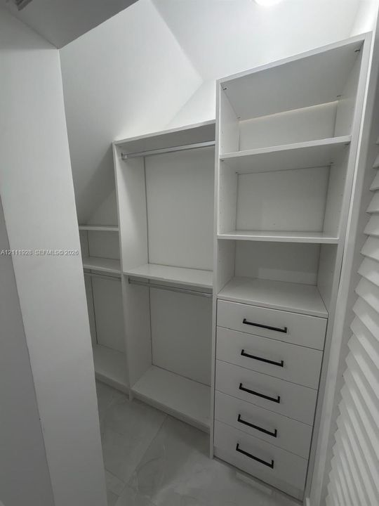 Custom walk-in closet featuring white built-in shelving, a five-drawer dresser unit, hanging rods, and matte black hardware