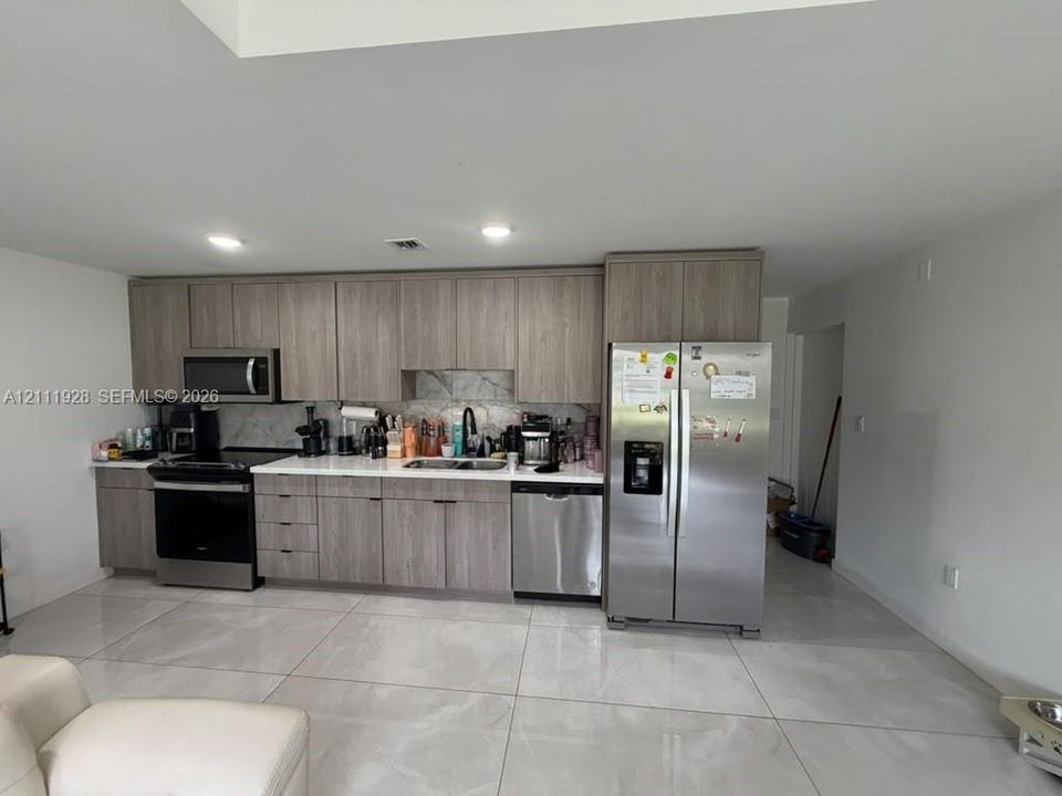 Kitchen featuring wood-finish cabinetry, solid surface countertops, stainless steel appliances, and large-format tile flooring