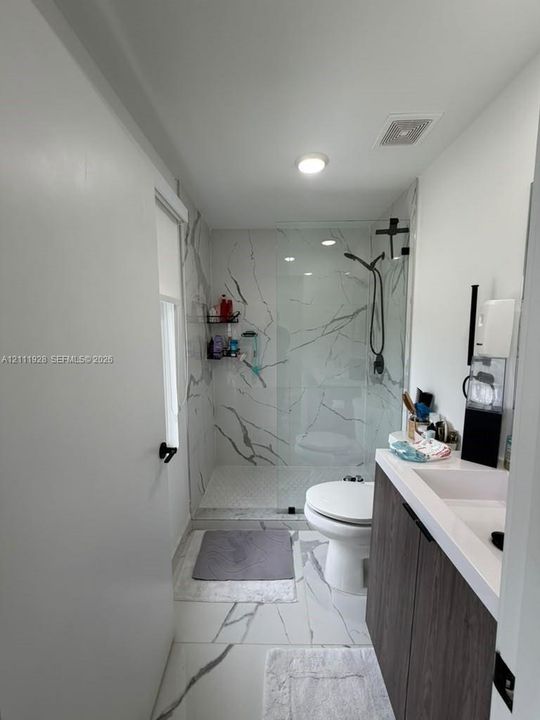 Bathroom featuring large-format tile flooring with marble-finish veining, a walk-in shower with a frameless glass enclosure, and a wood-finish vanity with a white countertop