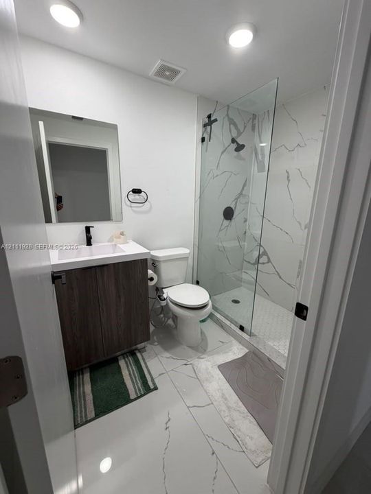 Bathroom featuring a glass-enclosed shower with floor-to-ceiling stone-style wall tile, white vanity with dark wood-finish cabinetry, rectangular vessel sink, and matte black fixtures