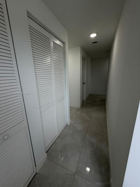 Hallway featuring large-format neutral tile flooring, white walls, and built-in closet cabinetry with louvered doors