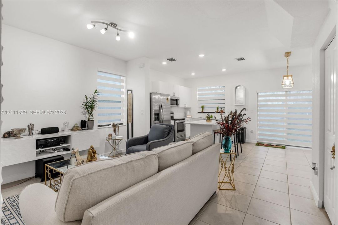 Open-concept interior featuring large-format ceramic tile flooring, built-in cabinetry, recessed and track lighting, and sliding glass doors with horizontal blinds