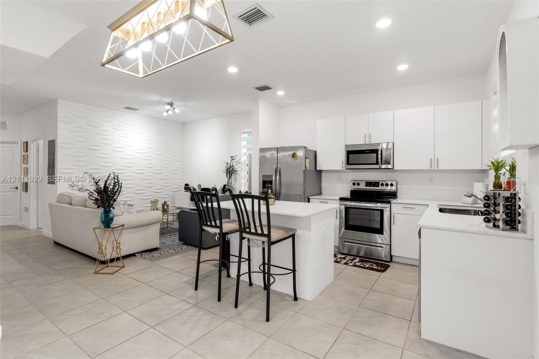 Kitchen featuring white cabinetry, stainless steel appliances, and a central island with quartz surfacing, highlighted by a textured accent wall and geometric pendant lighting