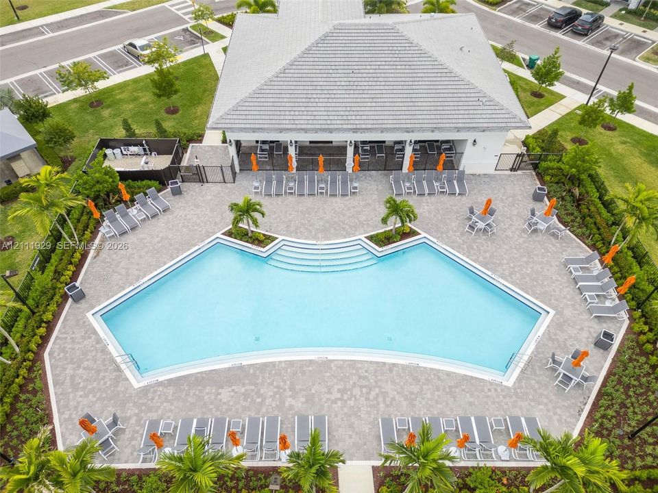 Community pool featuring a concrete paver deck, integrated step entry, perimeter landscaping, and a covered clubhouse pavilion