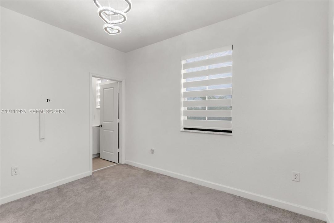 Interior room featuring neutral carpeting, a modern multi-tiered circular light fixture, and a window equipped with banded zebra-style roller shades