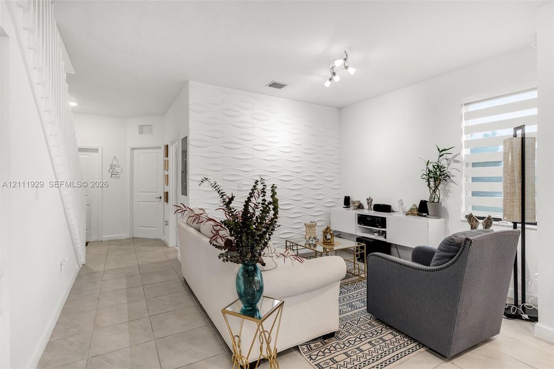 Textured accent wall featuring a dimensional wave pattern, neutral tile flooring, built-in media console, and dual-track lighting