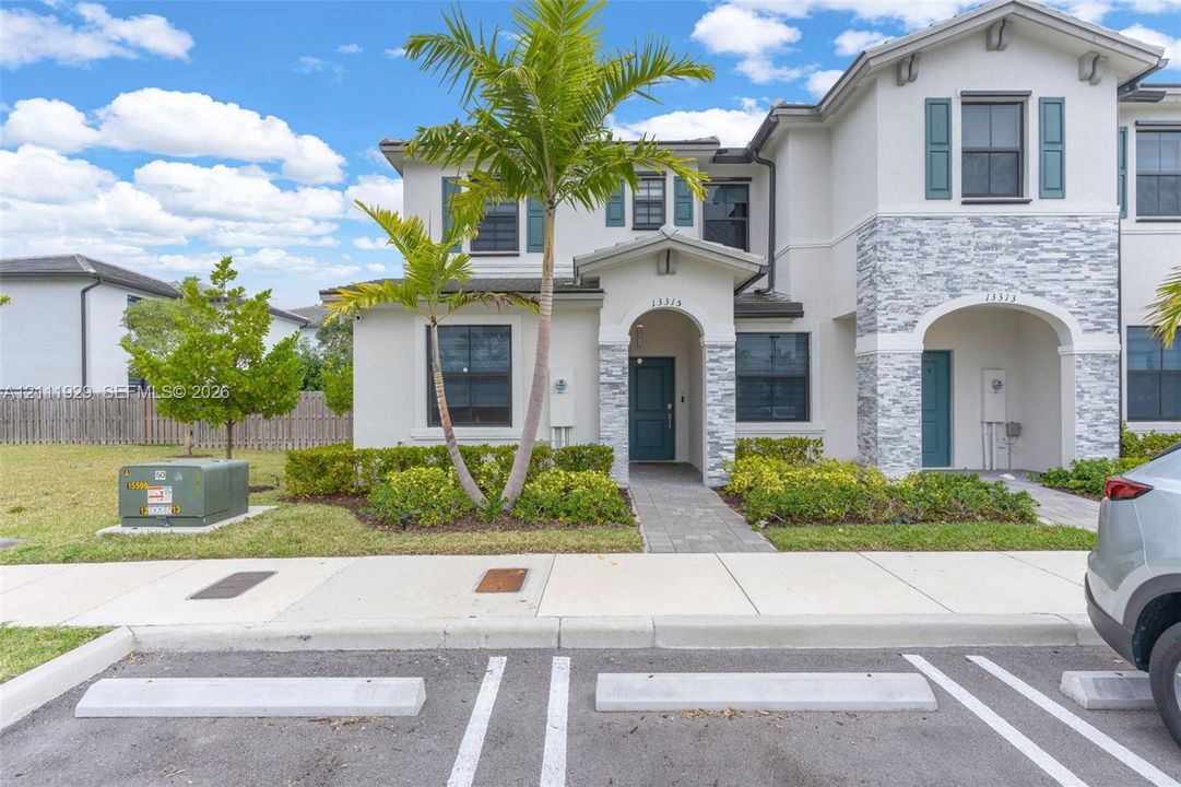 Two-story exterior featuring light-colored stucco finish, stacked stone veneer accents, arched entryways, and shuttered windows