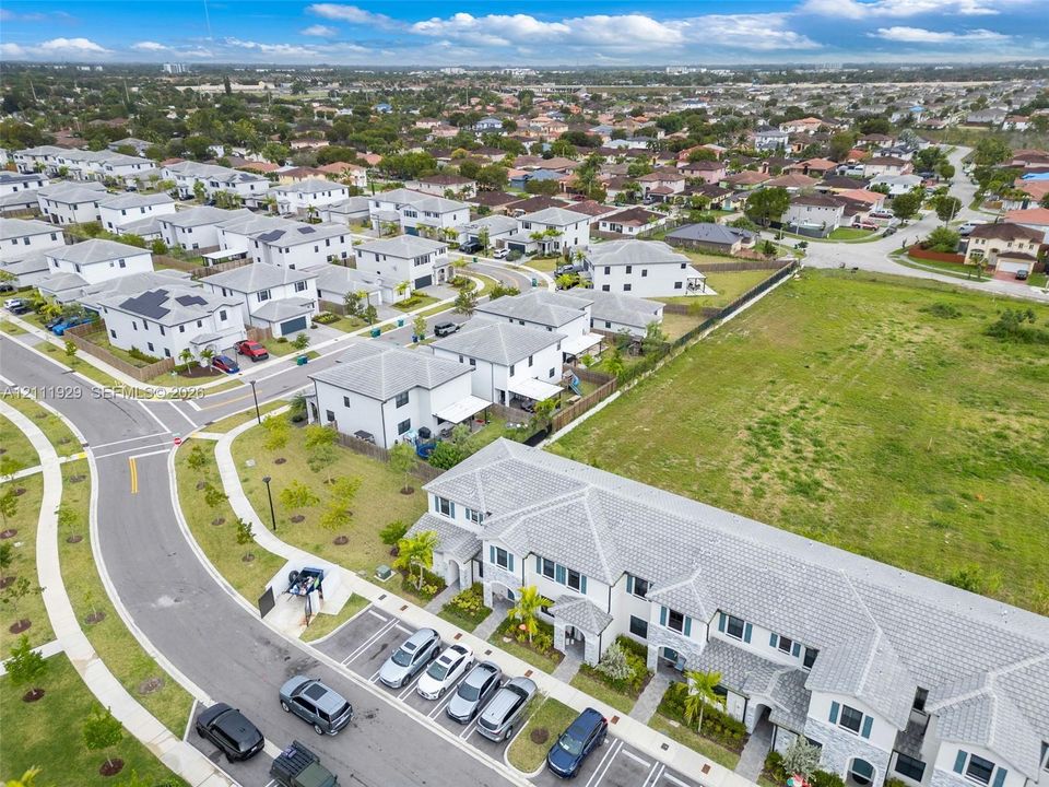 Aerial view of multi-unit residential property featuring a gray tile roof, light-toned stucco exterior, and dedicated surface parking