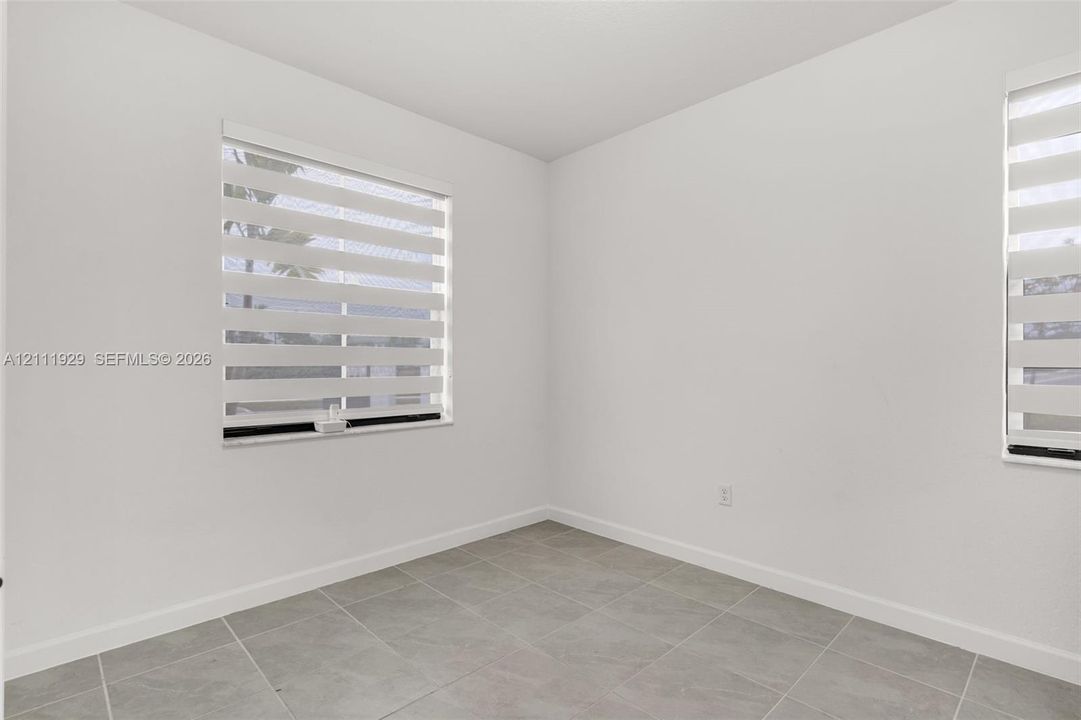 Neutral-toned ceramic tile flooring, crisp white walls, and dual windows equipped with horizontal light-filtering shades