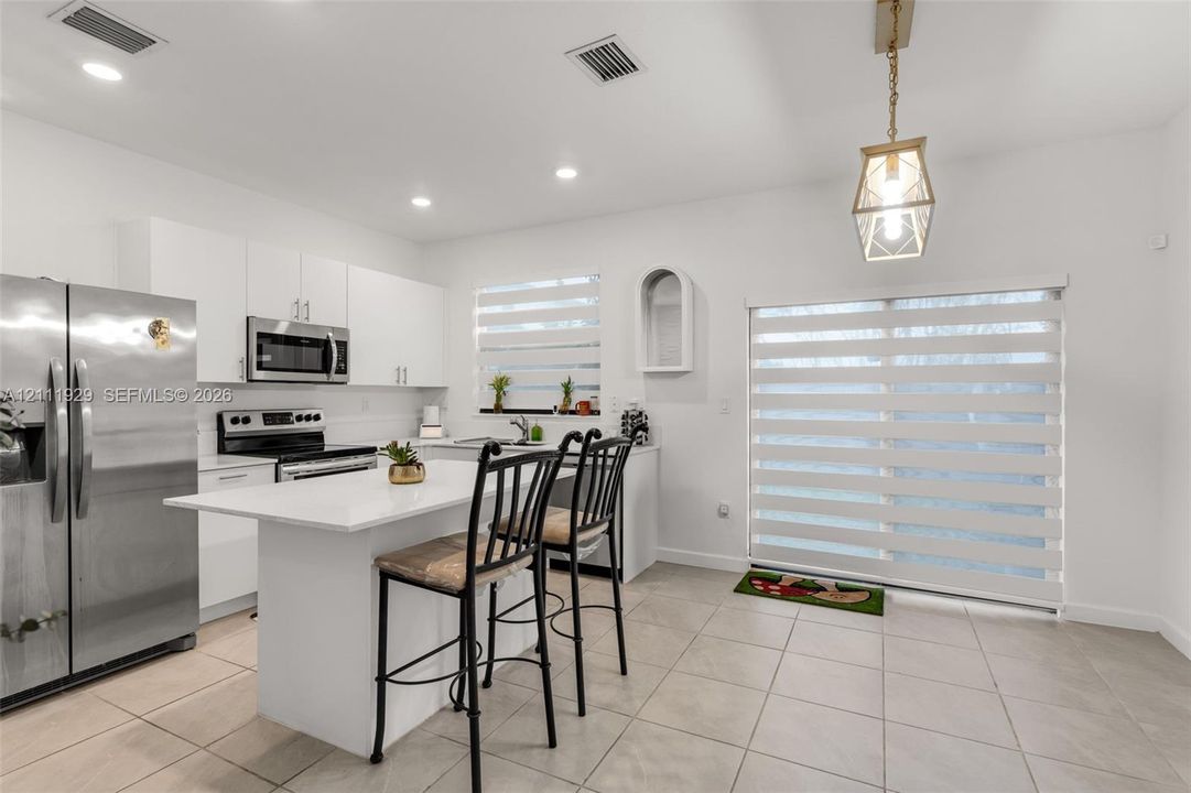 Kitchen featuring flat-panel white cabinetry, a center island with a stone-finish countertop, stainless steel appliances, recessed lighting, and large-format tile flooring