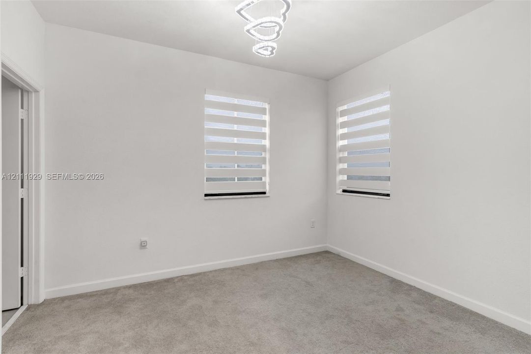 Neutral-toned interior space featuring carpeting, dual windows with installed light-filtering zebra blinds, and a contemporary multi-ring LED flush-mount fixture