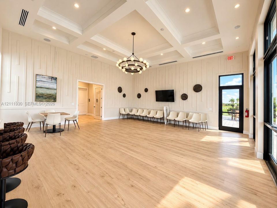 High-ceiling interior space featuring a coffered ceiling, wood-finish flooring, full-wall vertical wood paneling, a large tiered multi-light chandelier, and floor-to-ceiling glass-paneled exterior door