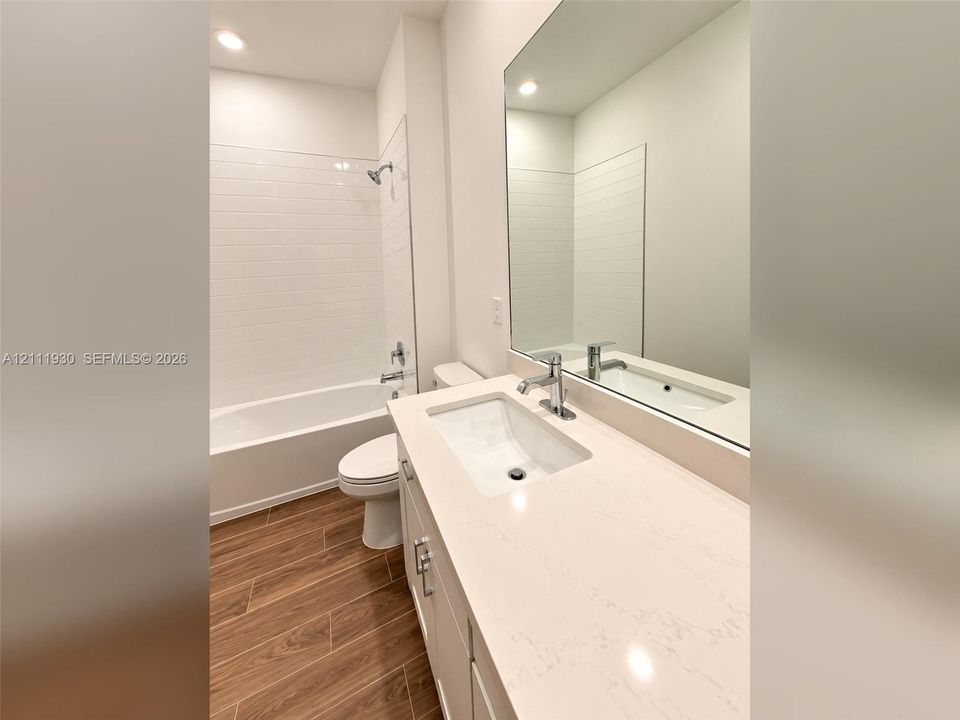 Bathroom featuring a vanity with a light-toned solid surface countertop and undermount sink, wood-finish flooring, full-width vanity mirror, and a tub-shower combination with white subway-style wall tile