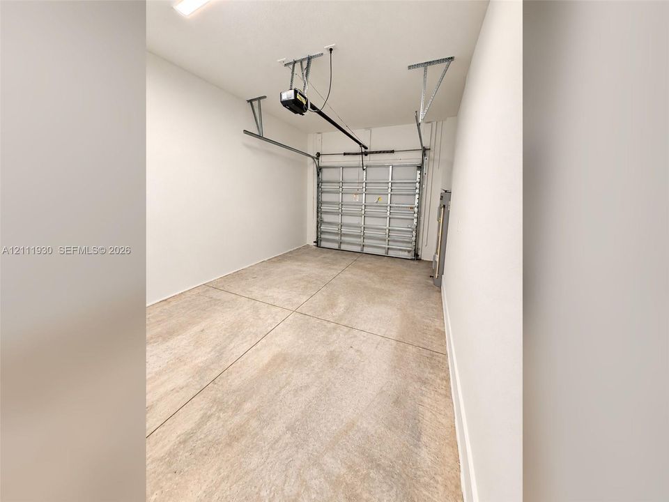Enclosed garage with concrete flooring, finished white walls, and a metal sectional overhead door featuring an automatic belt-drive opener