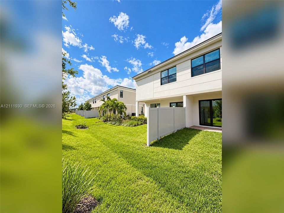 Two-story exterior featuring light-toned smooth stucco siding, black-framed windows, sliding glass doors, and a private vinyl privacy fence