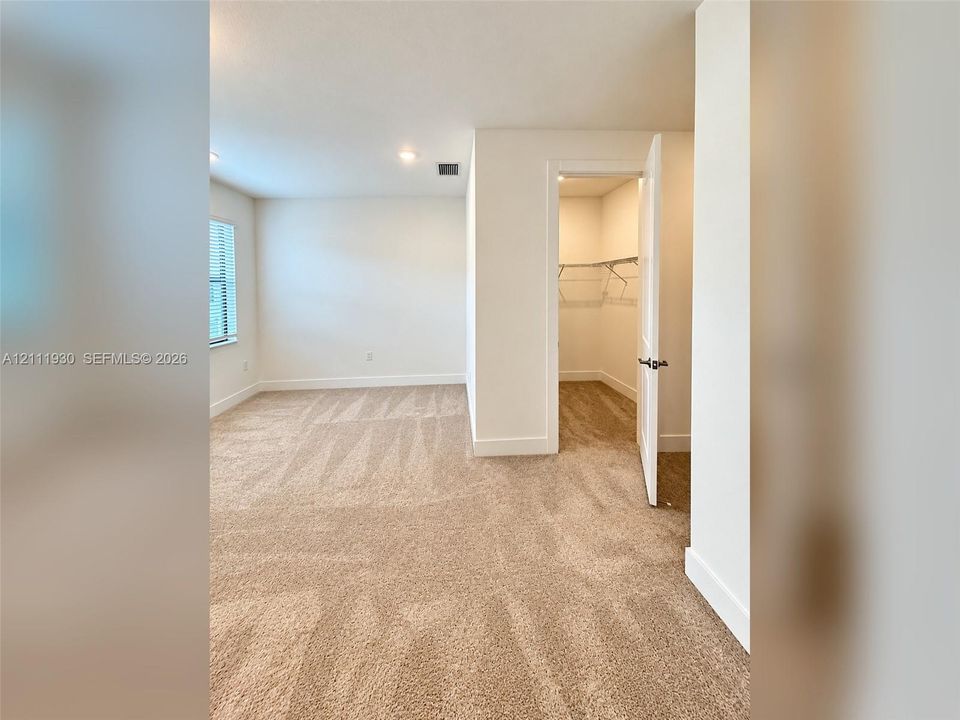 Neutral-toned wall-to-wall carpeting, recessed ceiling lighting, and a walk-in closet featuring built-in wire shelving