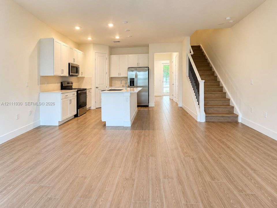 Kitchen featuring white cabinetry, center island, wood-finish flooring, and a staircase with wooden treads and a dark metal railing