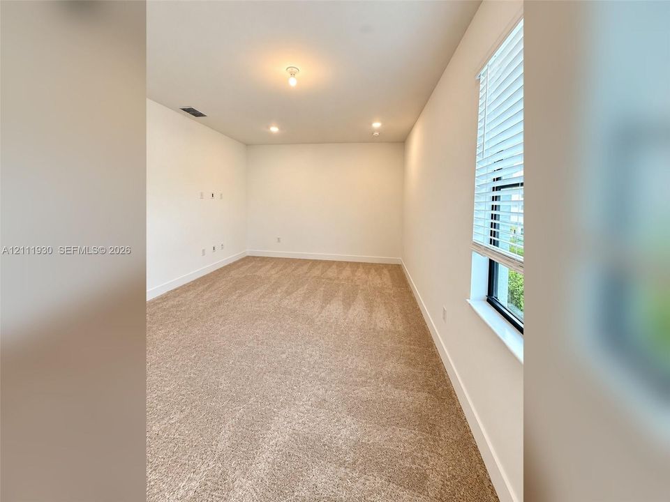 Neutral interior space featuring wall-to-wall carpeting, recessed ceiling lighting, and a window fitted with horizontal blinds