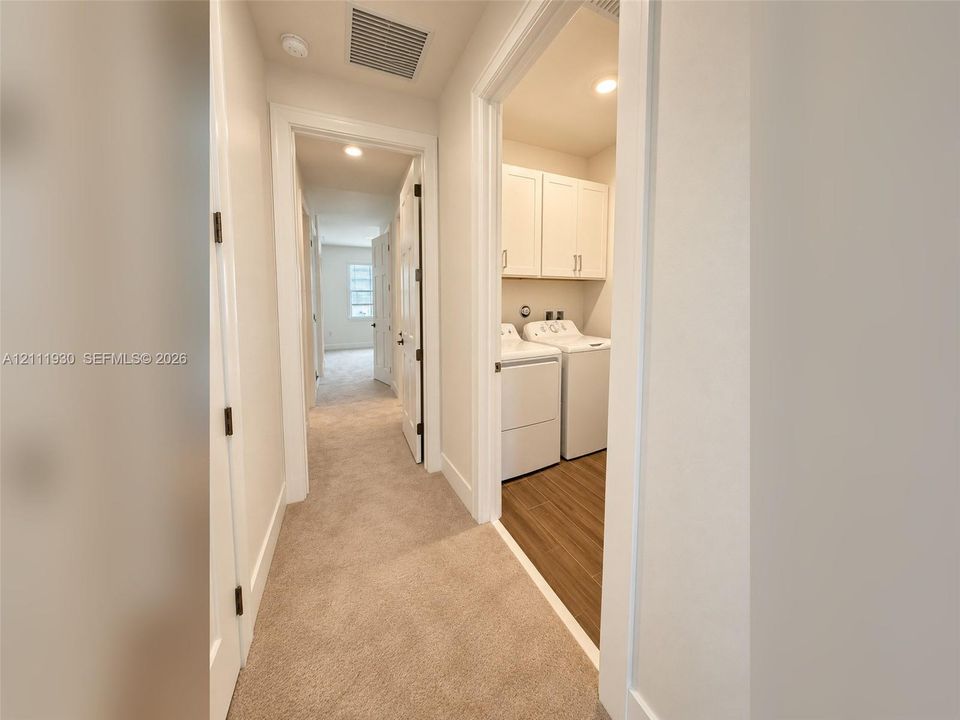 Laundry area featuring built-in upper cabinetry and wood-finish flooring, hall with neutral carpeting, and recessed lighting