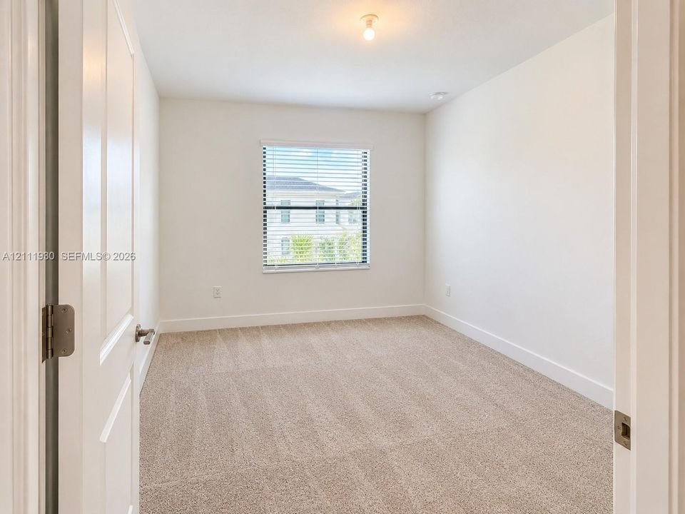 Neutral-toned wall-to-wall carpeting, single-hung window with horizontal blinds, and two-panel interior door