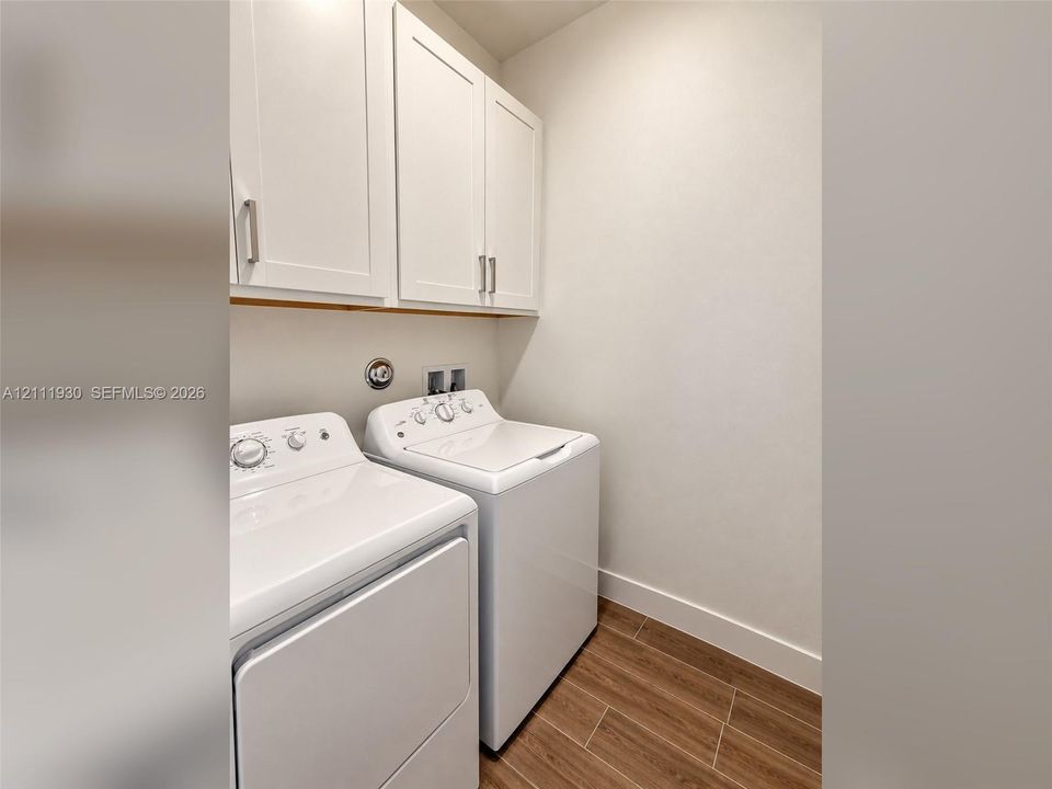 Laundry room featuring wood-finish tile flooring and white shaker-style cabinetry with satin nickel hardware