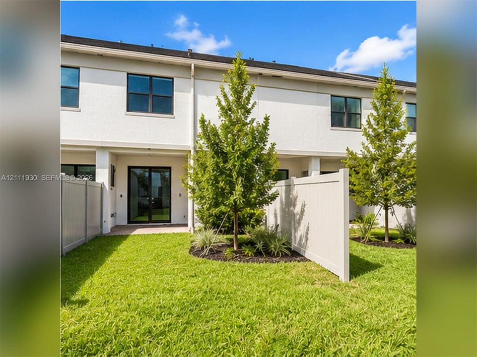 Stucco exterior with sliding glass doors, private fenced rear yard, and manicured green space with mature landscaping