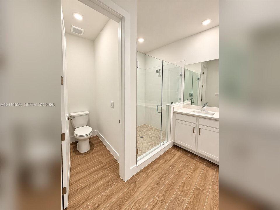 Bathroom featuring wood-finish flooring, white cabinetry, a glass-enclosed shower, a polished-edge mirror, and recessed lighting