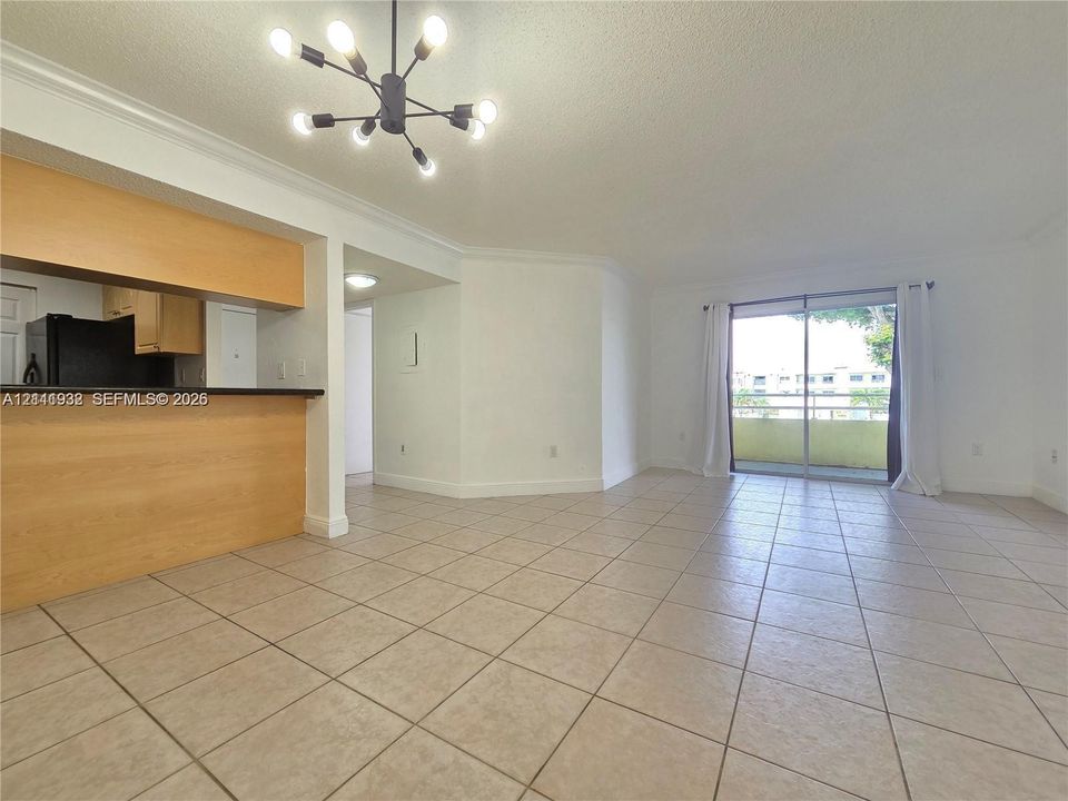 Open-concept living space featuring ceramic tile flooring, a breakfast bar with light wood-finish cabinetry, a multi-arm modern light fixture, and sliding glass doors with balcony access