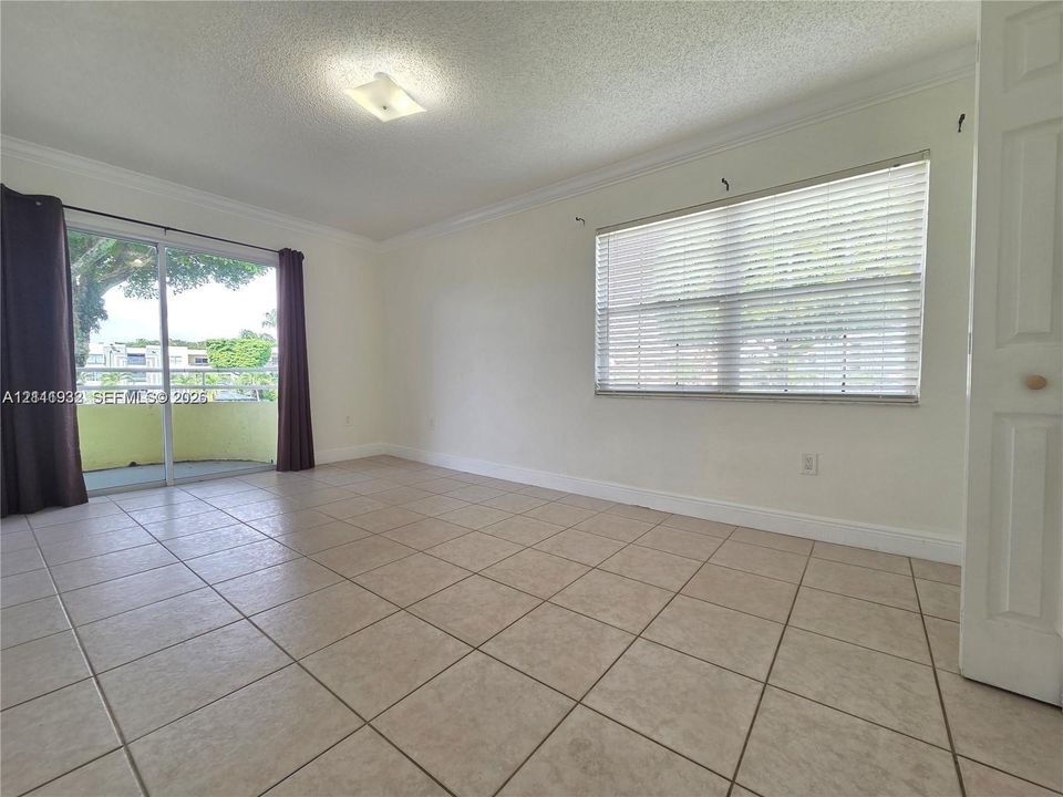 Interior space featuring ceramic tile flooring, crown molding, sliding glass doors, horizontal window blinds, and a flush-mount ceiling light fixture