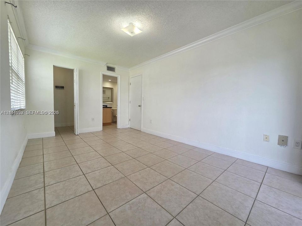 Neutral-toned tile flooring, flush-mount ceiling lighting, crown molding, and horizontal slatted window blinds