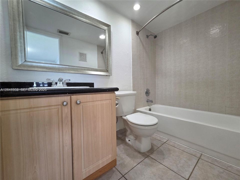 Bathroom featuring a vanity with light-tone wood cabinetry, black countertop, rectangular drop-in sink, large wall-mounted mirror, and tile flooring