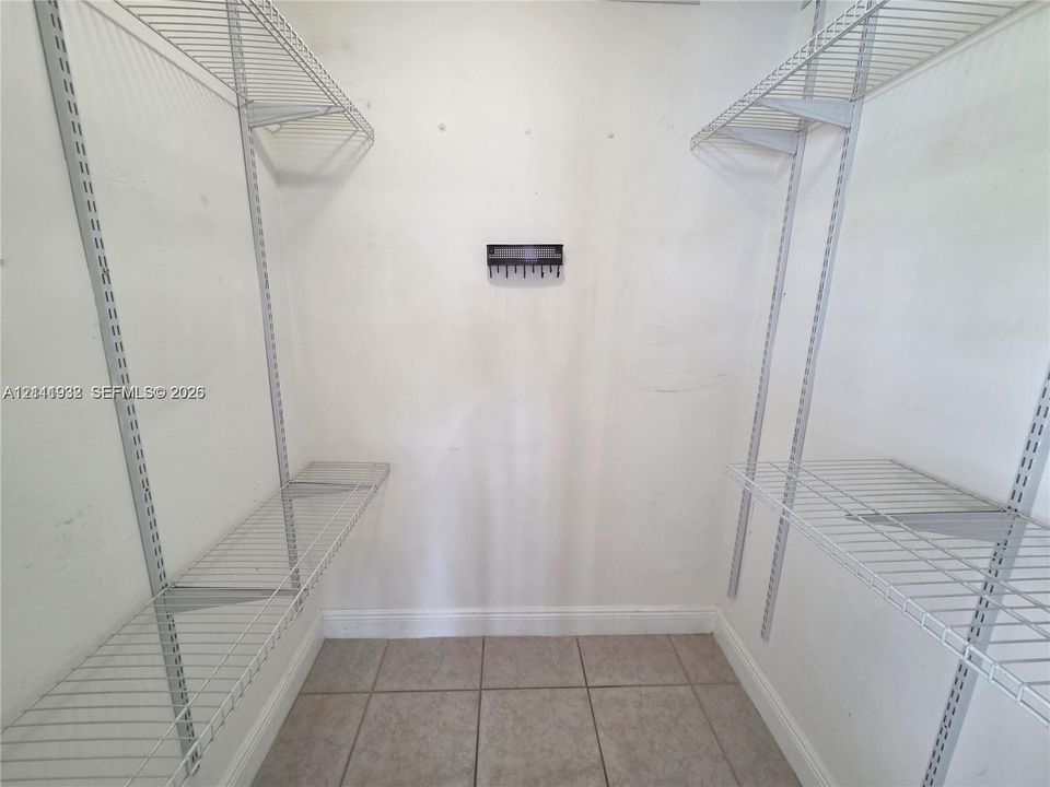 Walk-in closet featuring tiled flooring, white walls, and dual-level wire shelving systems with integrated vertical adjustment tracks