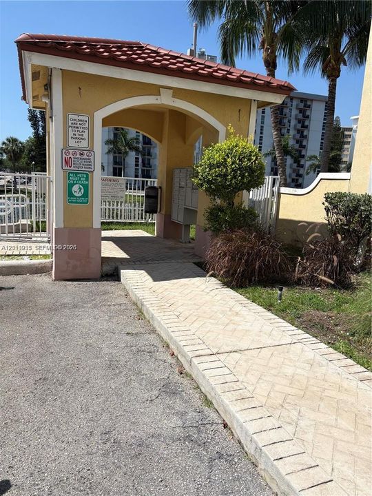 Covered entrance featuring a red tile roof, stucco archway, built-in central mailboxes, and a herringbone-patterned paver walkway