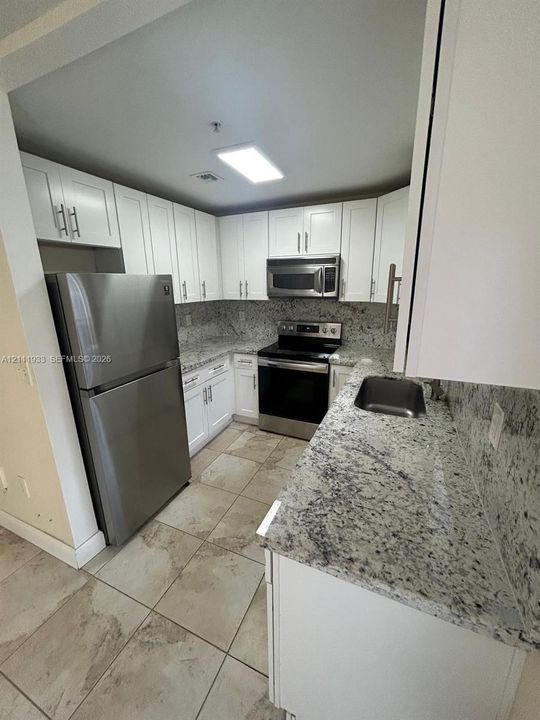 Kitchen featuring white shaker-style cabinetry, stone countertops, integrated stainless steel appliances, and tile flooring