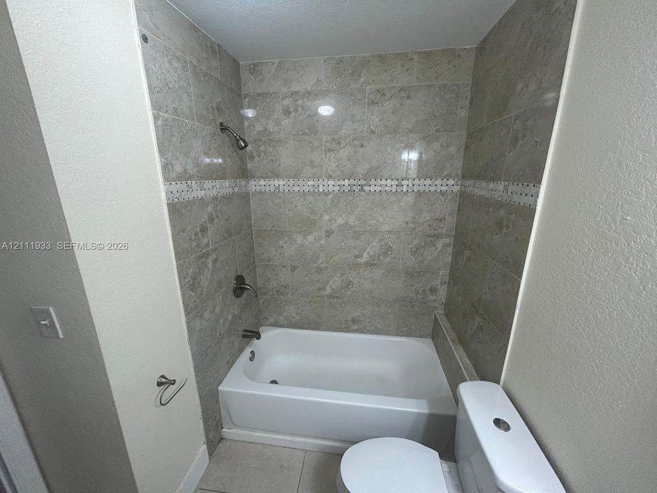 Tub and shower combination featuring neutral-toned wall tile, a decorative stone-patterned accent border, and metallic fixtures