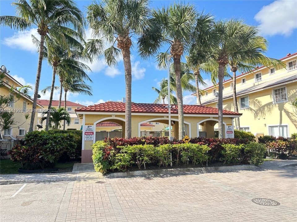 Outdoor pavilion featuring a red tile roof, arched architectural details, paved hardscaping, and surrounding mature palm trees and manicured landscaping