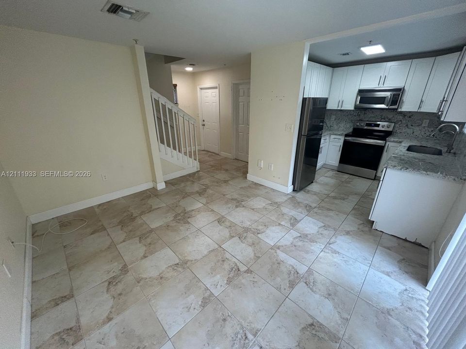 Kitchen featuring white cabinetry, stone-finish countertops, and stainless steel appliances, set against stone-finish floor tiling and a staircase with white balusters