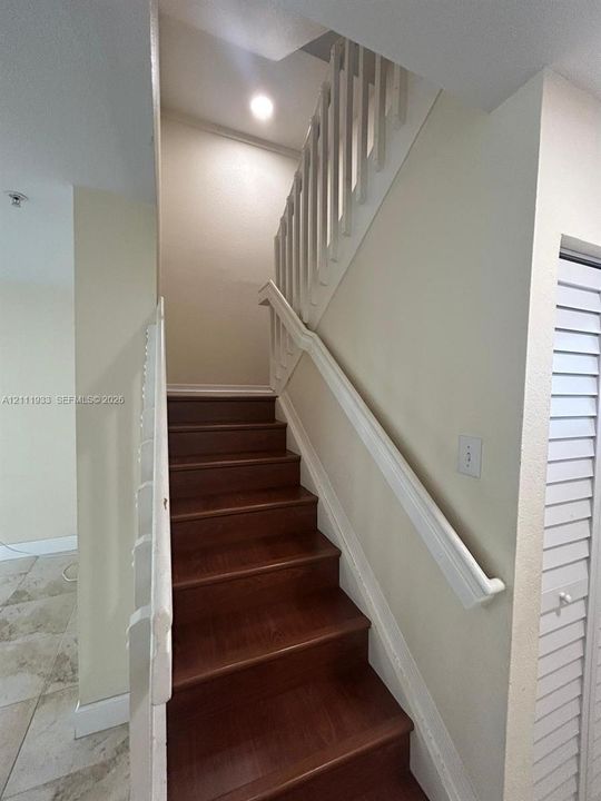 Staircase featuring wood-finish treads, white painted balustrades, a white handrail, and a louvered closet door