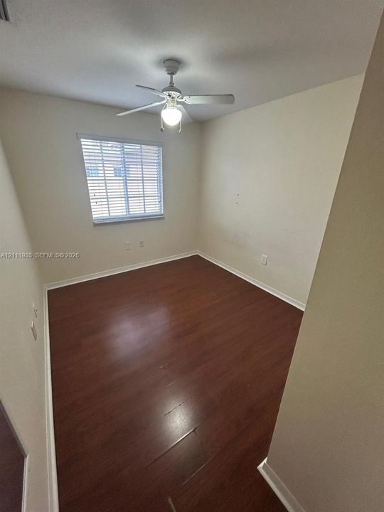 Room featuring wood-finish flooring, a white ceiling fan with integrated lighting, and a single window with horizontal blinds
